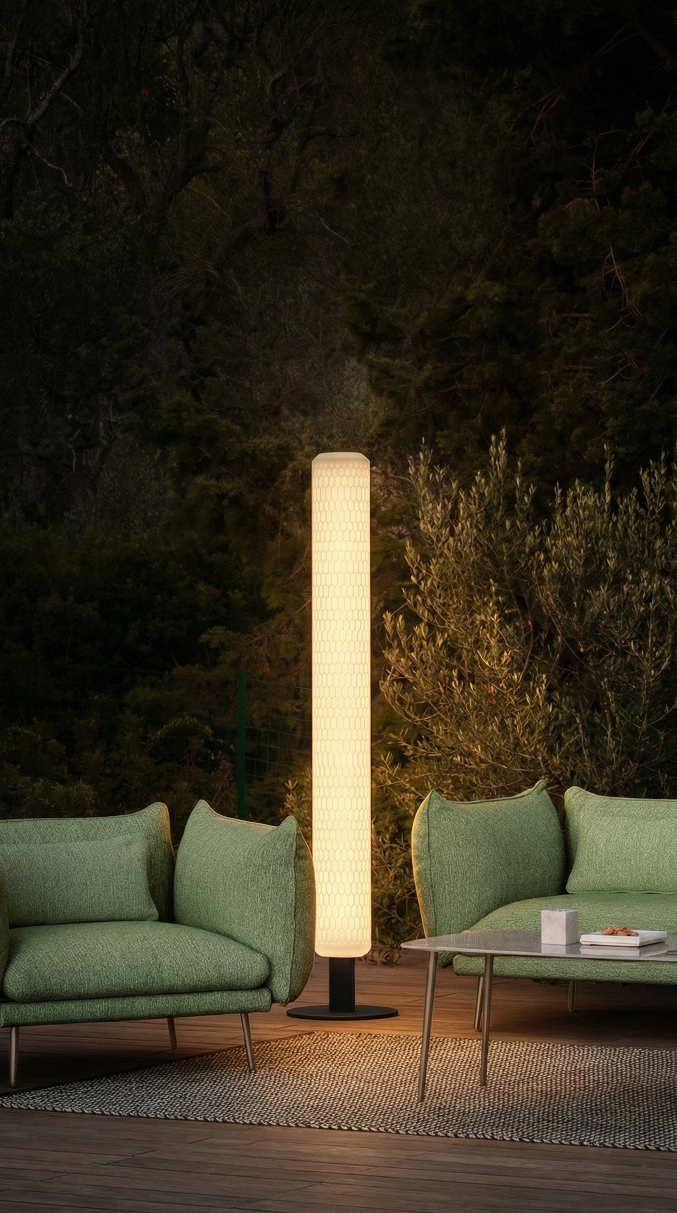 Outdoor setting with green sofas and a tall cylindrical lamp in a dark forested area.