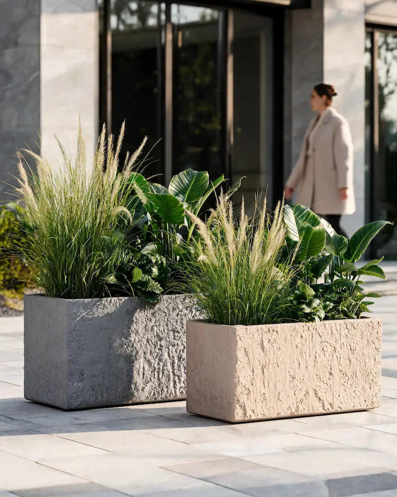 Two stone planters with green plants on a patio area in front of a modern building.